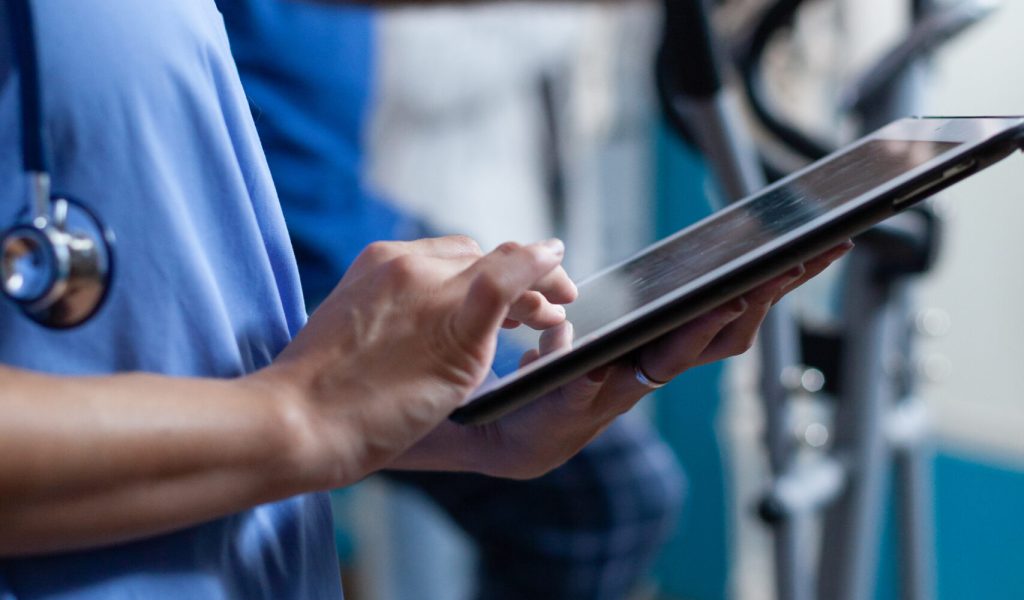 Close up of medical assistant touching tablet display to help elder people with physical recovery. Nurse using gadget with touch screen for healthcare and physiotherapy for strength